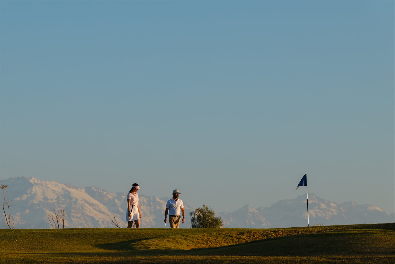 Golfers on a fairway with the Atlas mountains beyond